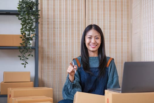 Happy young Asian woman entrepreneur, Smile for sales success after checking order from online shopping store in a laptop at home office, Concept of merchant business online and eCommerce..