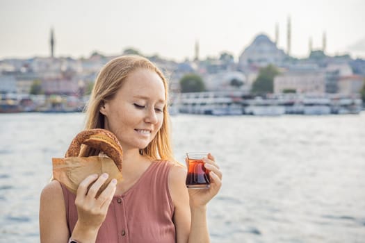 Woman in Istanbul having breakfast with Simit and a glass of Turkish tea. Glass of Turkish tea and bagel Simit against golden horn bay in Istanbul, Turkey. Turkiye.