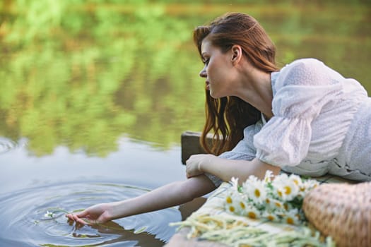 a woman in a light dress lying on a pier by the lake touches the water. High quality photo