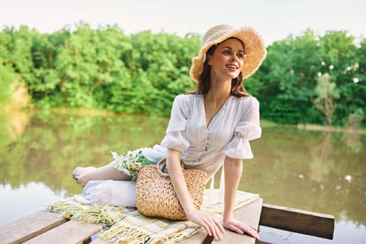 happy woman in a wicker hat resting in nature by the lake in summer. High quality photo