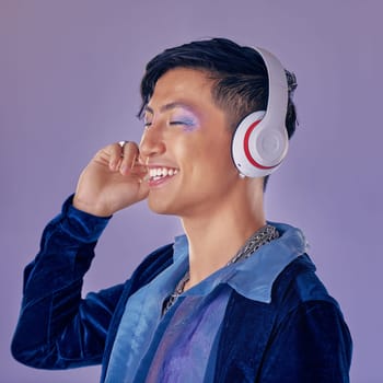 Music, makeup and cyberpunk with an asian man model in studio on a purple background for lgbt freedom. Future, happy and fashion with a handsome young androgynous male streaming or listening to audio.