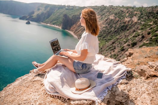 Freelance woman working on a laptop by the sea, typing away on the keyboard while enjoying the beautiful view, highlighting the idea of remote work