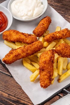 Chicken fingers and french fries with sauces on wooden table