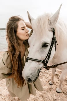 A white horse and a woman in a dress stand on a beach, with the sky and sea creating a picturesque backdrop for the scene