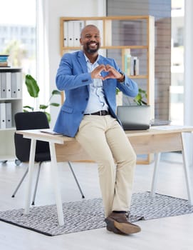 African businessman, heart sign or office for smile, happiness or sitting on desk with love. Black man, corporate executive or finance job with hands signal, care or solidarity for support in Atlanta.