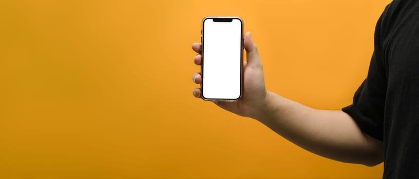 Hand holding mockup smartphone over yellow background. Empty screen for your webpage or advertise text.