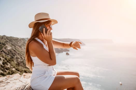 Successful business woman in yellow hat working on laptop by the sea. Pretty lady typing on computer at summer day outdoors. Freelance, travel and holidays concept.