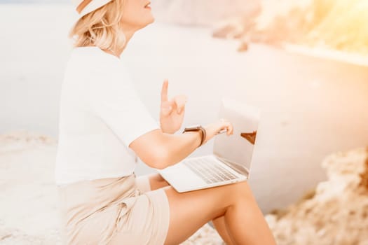 Digital nomad, Business woman working on laptop by the sea. Pretty lady typing on computer by the sea at sunset, makes a business transaction online from a distance. Freelance remote work on vacation