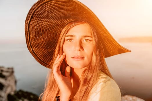 Portrait of happy young woman wearing summer black hat with large brim at beach on sunset. Closeup face of attractive girl with black straw hat. Happy young woman smiling and looking at camera at sea