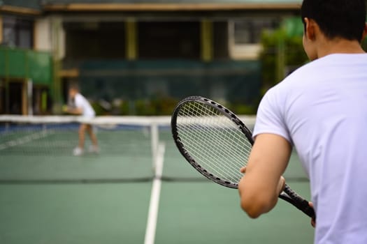 Back view of tennis player standing in ready position to receive a serve, practicing for competition on a court.