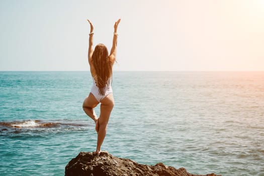 Woman sea yoga. Back view of free calm happy satisfied woman with long hair standing on top rock with yoga position against of sky by the sea. Healthy lifestyle outdoors in nature, fitness concept