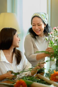 Shot of young asian woman and senior mother making a bouquet with fresh flowers at floral shop. Small business concept.