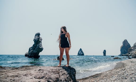 Woman travel sea. Young Happy woman in a long red dress posing on a beach near the sea on background of volcanic rocks, like in Iceland, sharing travel adventure journey