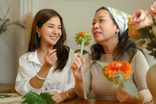 Happy young asian woman and senior mother making a bouquet with fresh flowers at floral shop. Small business concept.