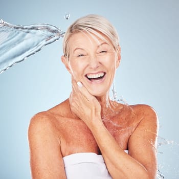 Smile, shower and portrait of a woman with a water splash isolated on a blue background in studio. Grooming, hygiene and face of an excited senior model with body and self care on a backdrop.