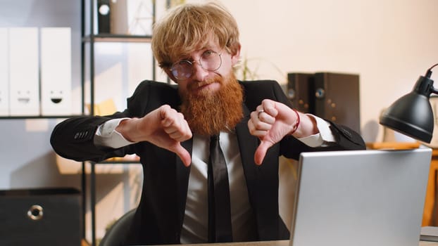 Dislike. Upset young businessman guy working on laptop computer at home office thumbs down sign gesture, expressing discontent, disapproval, dissatisfied bad work. Displeased serious freelancer man