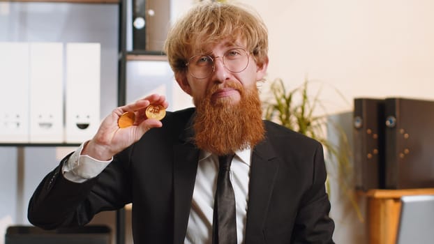 Young bearded businessman stock trader earning bitcoins after online monitoring trading operations. Increasing wealth, financial prosperity. Freelancer man working on laptop at home office workplace