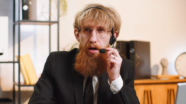 Businessman wearing headset, freelance worker, call center or support service operator helpline, having talk with client, colleague, communication support at office workplace. Professional manager man