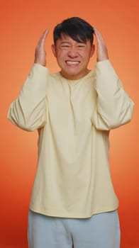 Handsome asian man feeling hopelessness loneliness, nervous breakdown, loses becoming surprised by lottery results, bad fortune, loss, unlucky news. Guy isolated on orange background. Vertical