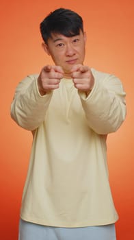 I choose you. Asian man pointing to camera and looking with playful happy expression, making choice, showing direction, hiring on work job. Guy on orange background. People lifestyles. Vertical