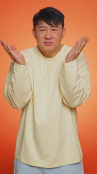 What Why. Sincere irritated asian man raising hands in indignant expression asking reason of failure demonstrating disbelief irritation by trouble. Confused guy on orange background. Vertical