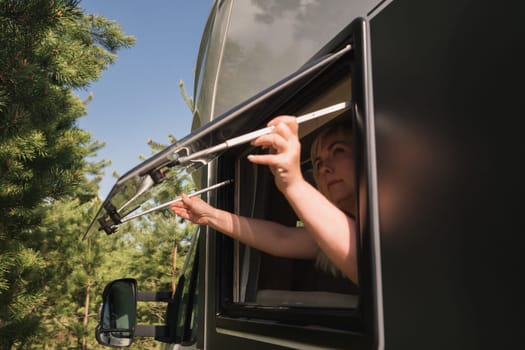 The girl opens the window of the van to enjoy the sun. The concept of people traveling on summer holidays inside a car-camping, mobile home.