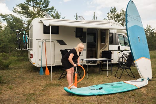 A woman inflates a sup-board for swimming near her motorhome.