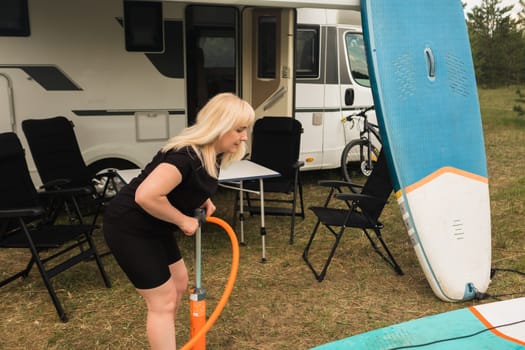 A woman inflates a sup-board for swimming near her motorhome.