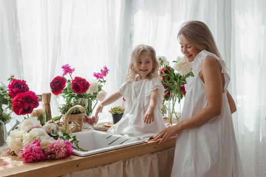 A little blonde girl with her mom on a kitchen countertop decorated with peonies. The concept of the relationship between mother and daughter. Spring atmosphere