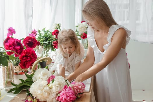 A little blonde girl with her mom on a kitchen countertop decorated with peonies. The concept of the relationship between mother and daughter. Spring atmosphere