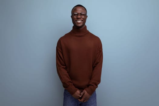 elegant young african brunet male businessman in stylish brown sweater and glasses on studio background with copy space.