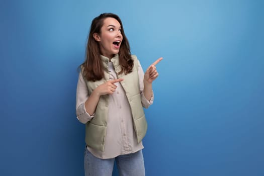 positive young brunette lady showing inspiration with hand on studio background with copy space.