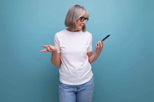 gray-haired mature woman studying digital technology smartphone on a bright studio background.