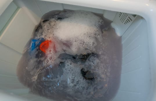 Dirty clothes in top loading washing machine. Clothes with bubble of laundry detergent in washing machine. Laundry concept. Top load washer. Housework. Washing machine and dirty water from cleaning.
