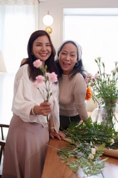 Startup, small business, flower shop. Young and older woman florist putting a flower on a vase.