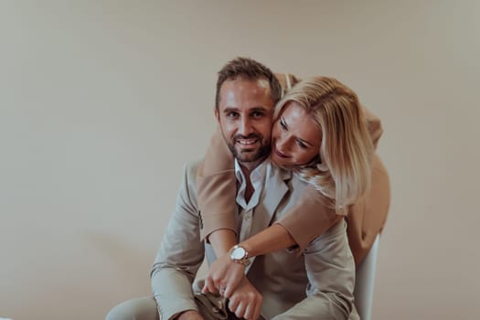 A business couple poses for a photograph together against a beige backdrop, capturing their professional partnership and creating a timeless image of unity and success