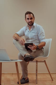 A confident businessman sitting and using tablet with a determined expression, while a beige background enhances the professional atmosphere, showcasing his productivity and expertise
