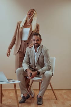 A business couple poses for a photograph together against a beige backdrop, capturing their professional partnership and creating a timeless image of unity and success