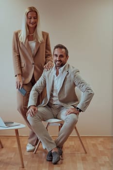 A business couple poses for a photograph together against a beige backdrop, capturing their professional partnership and creating a timeless image of unity and success