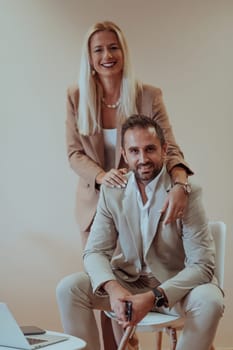 A business couple poses for a photograph together against a beige backdrop, capturing their professional partnership and creating a timeless image of unity and success