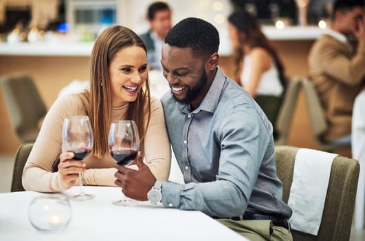 Cheers, love and couple on a date in a restaurant for valentines day, romantic event or anniversary. Happy, smile and interracial man and woman drinking wine, talking and bonding at a luxury dinner