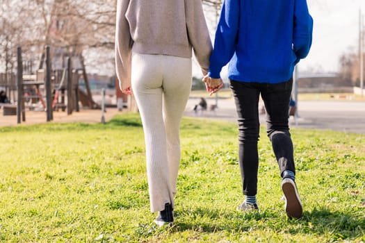 two unrecognizable women walking together holding hands in a city park, concept of freedom and love between people of the same sex