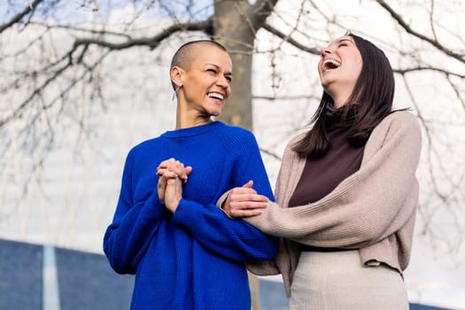 lesbian couple of two young women laughing happy during a romantic walk in a city park, concept of freedom and love between people of the same sex