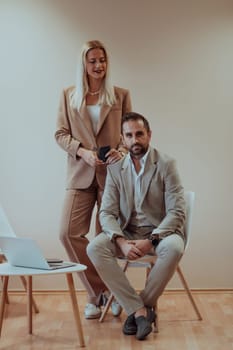 A business couple poses for a photograph together against a beige backdrop, capturing their professional partnership and creating a timeless image of unity and success