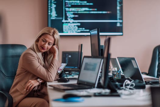 A businesswoman sitting in a programmer's office surrounded by computers, showing her expertise and dedication to technology