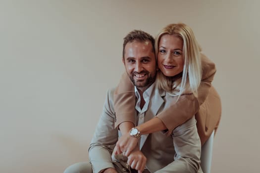 A business couple poses for a photograph together against a beige backdrop, capturing their professional partnership and creating a timeless image of unity and success