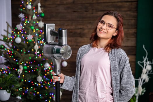 An attractive young girl holds a vacuum cleaner in her hand and smiles beautifully. It's time for a thorough cleaning of the whole house.