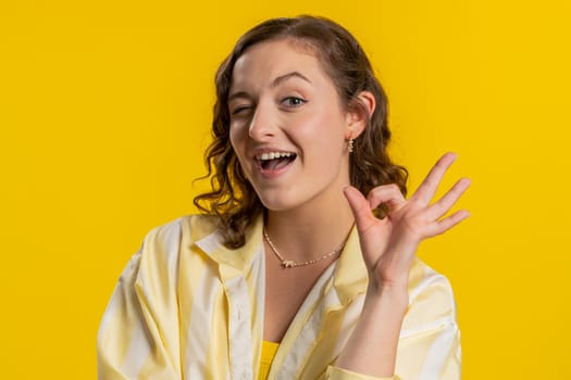 Okay. Joyful happy young woman looking approvingly at camera showing approve feedback gesture like Ok sign positive something good. Pretty girl isolated on yellow background. People sincere emotion
