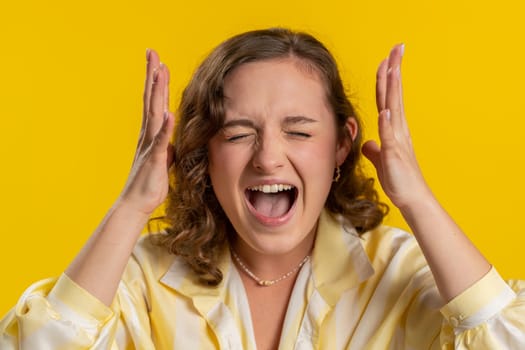 Young woman screams yell shout from stress tension problems feels horror hopelessness fear panic surprise shock expresses gestures rage. Pretty girl isolated on yellow studio background indoors