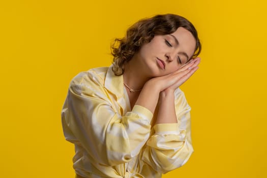 Tired sleepy young woman inattentive feeling somnolent lazy bored gaping suffering from lack of sleep, lying down on hands, relax. Exhausted girl isolated alone on yellow studio background. Lifestyles
